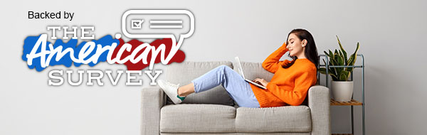 Backed by The American Survey. Young woman using laptop on loveseat.